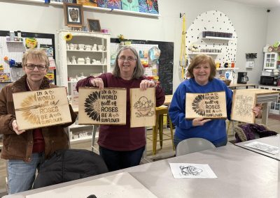 Three women showing their spring wood burning crafts